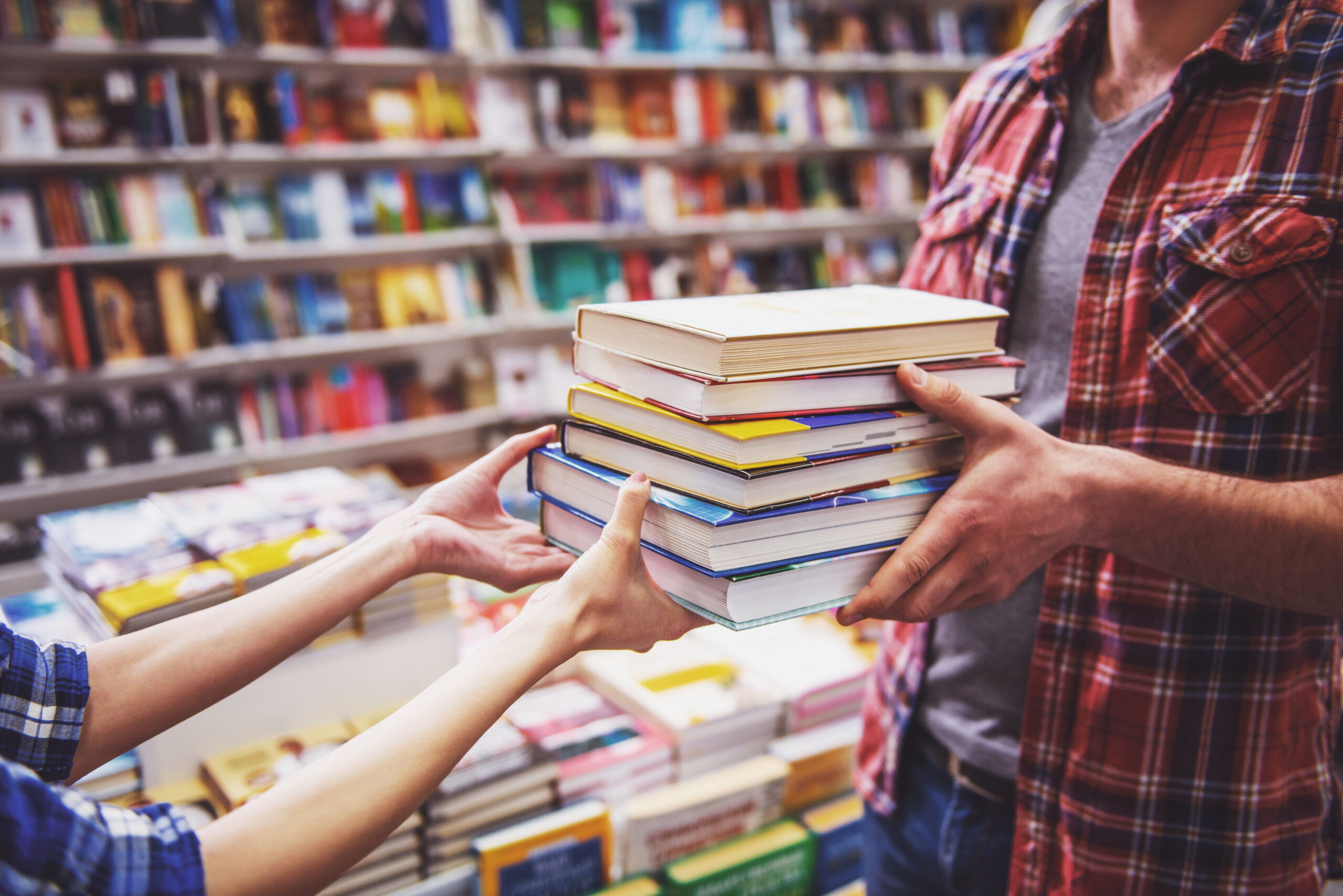 Cropped image of young man and woman holding a pile of books while standing in the book shop