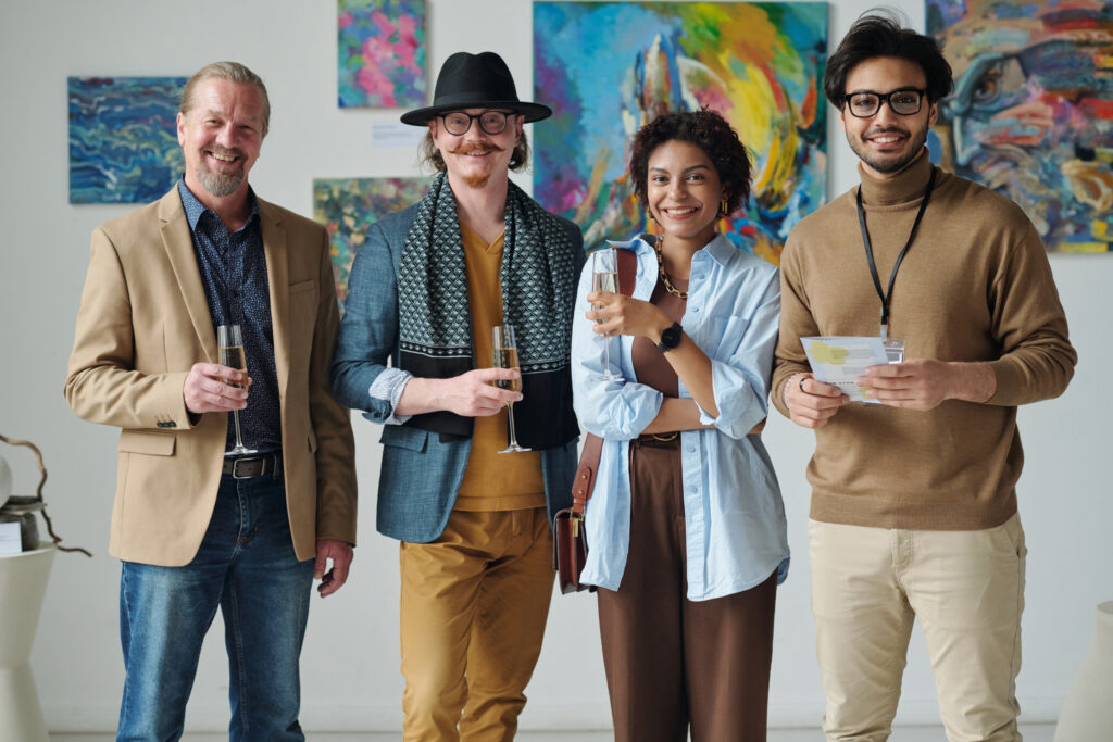 Portrait of group of people smiling at camera standing with glasses of champagne in art gallery