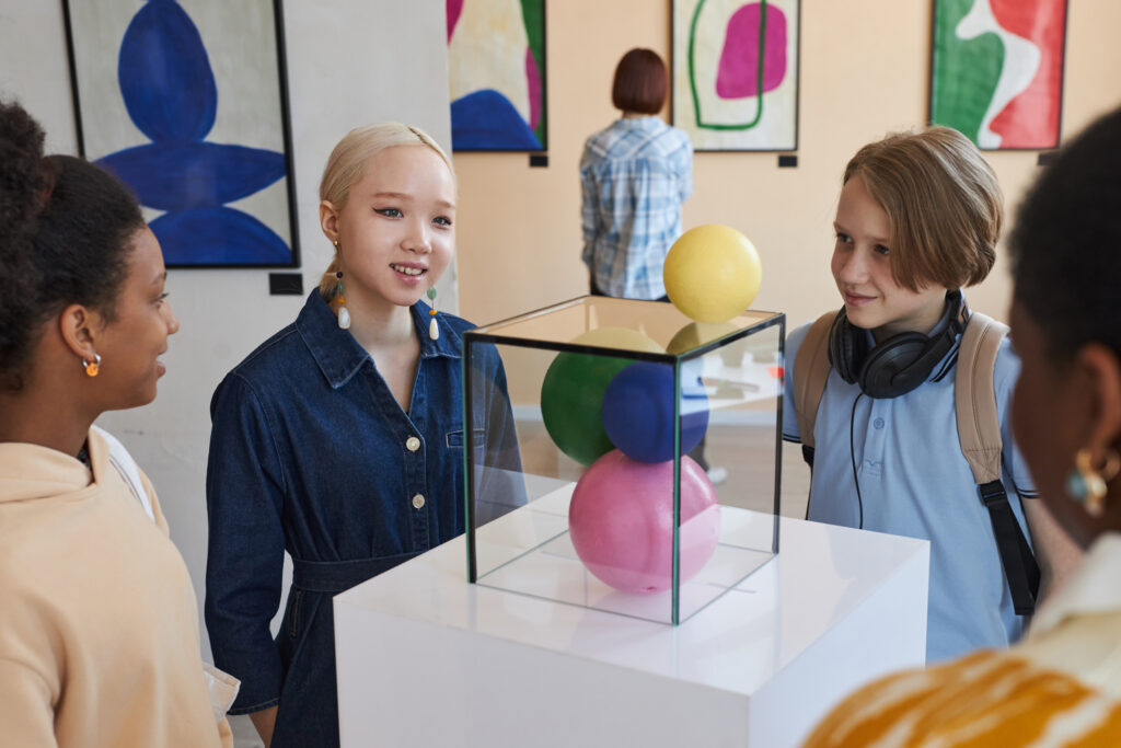 Diverse group of smiling teenage children looking at abstract sculptures in modern art gallery
