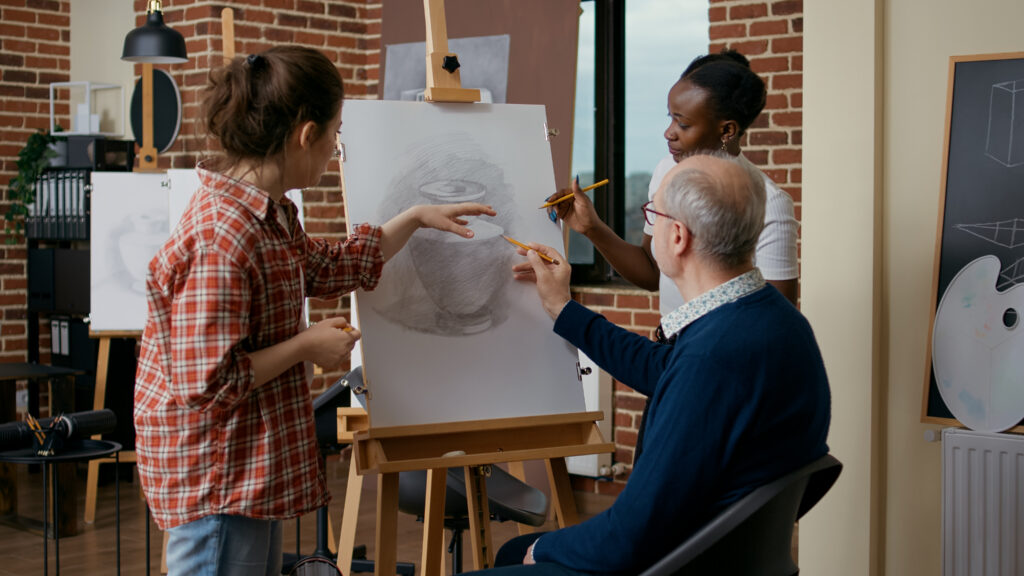 Teacher and student helping old man to draw vase on canvas, explaining drawing skills.