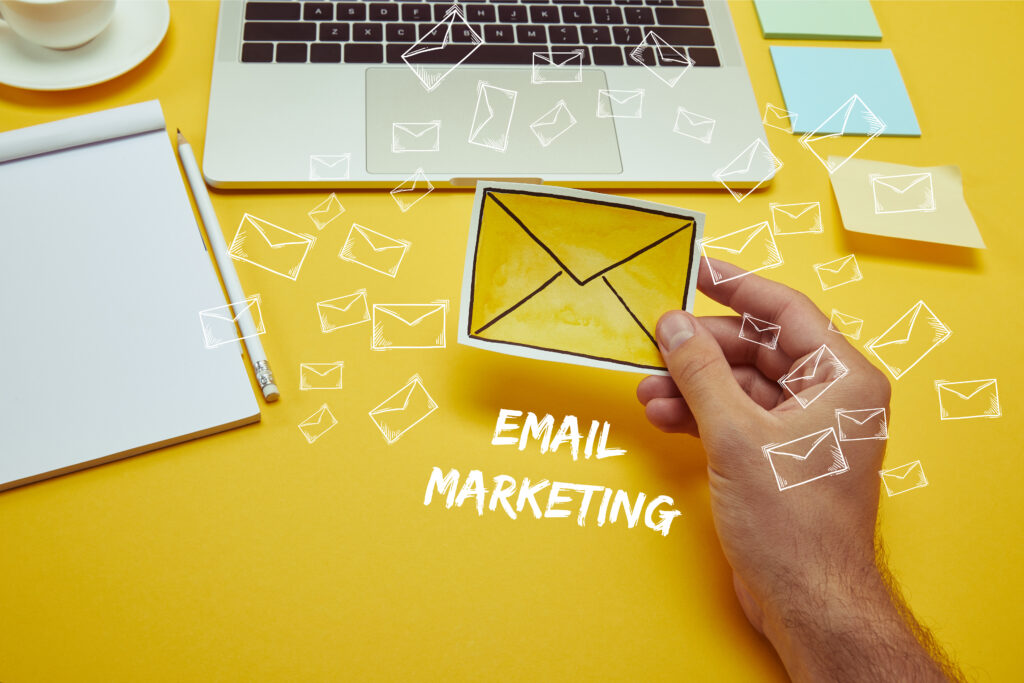 cropped image of man holding envelope sign near laptop with"email marketing" lettering and email