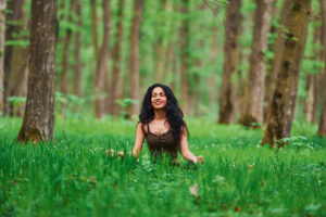 Positive brunette in casual clothes meditating in the forest at daytime